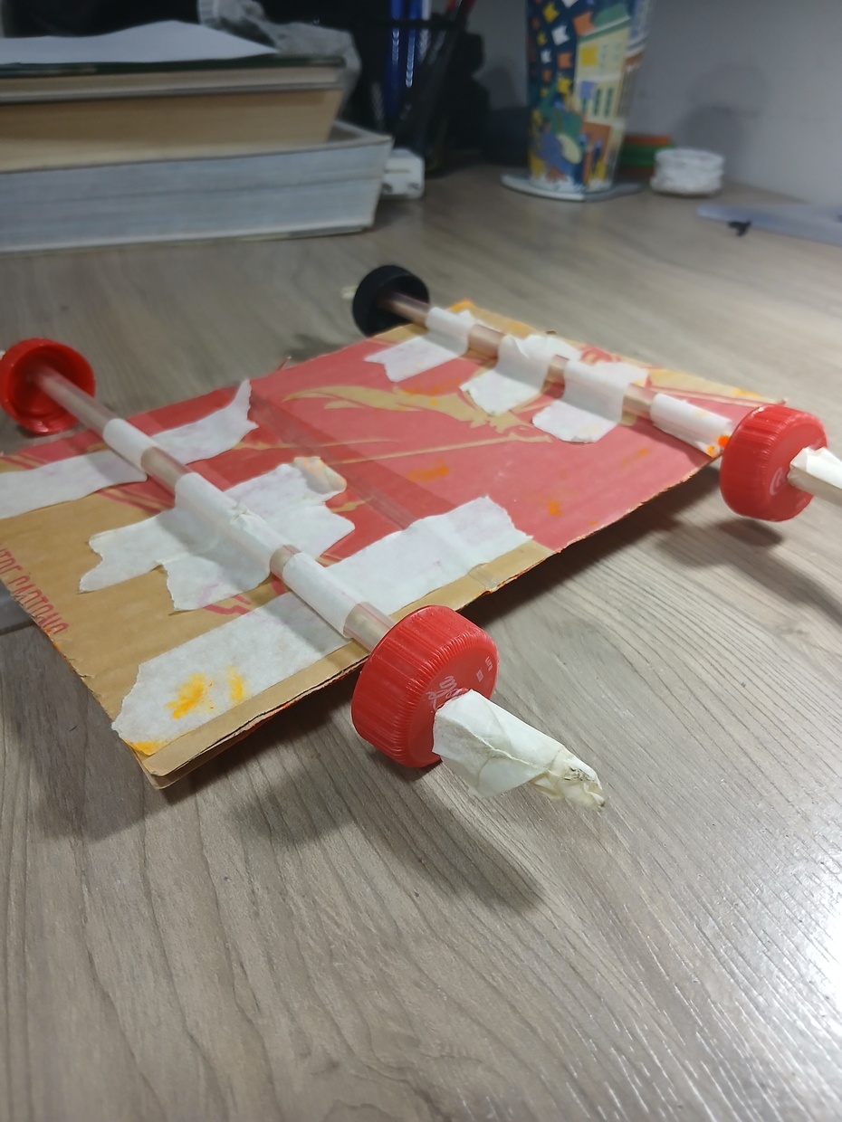 agora, coloque as 4 tampinhas em cada ponta dos canudos e cada parte que sobrar para fora dos palitos passe a fita nas pontas dos palitos, que irá servir para impedir de que a roda fique torta além de não deixá-la escapar