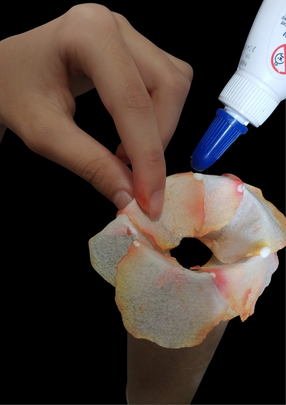 Coloque as pétalas uma sobrepondo a pontinha da outra na borda da parte de cima do tubo de papelão e vá colocando a cola líquida entre uma pétala e outra sempre no mesmo sentido e reserve uma pétala para próxima etapa.